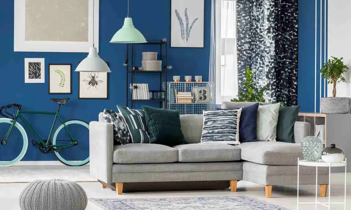 Un soggiorno moderno con divano grigio, pouf e tappeto, dominato da **colori freddi** come il blu intenso delle pareti e i toni verdi e blu degli accessori.