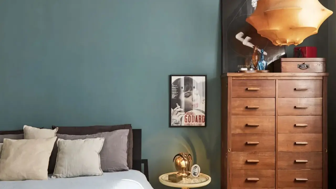 Un'elegante camera da letto con pareti color ottanio, un letto con cuscini in lino e un comò in legno. L'abbinamento colori camera da letto è sofisticato e rilassante.