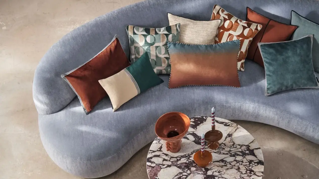 Tante idee cuscini divano: tonalità calde e fredde, fantasie geometriche e texture vellutate su un divano grigio.