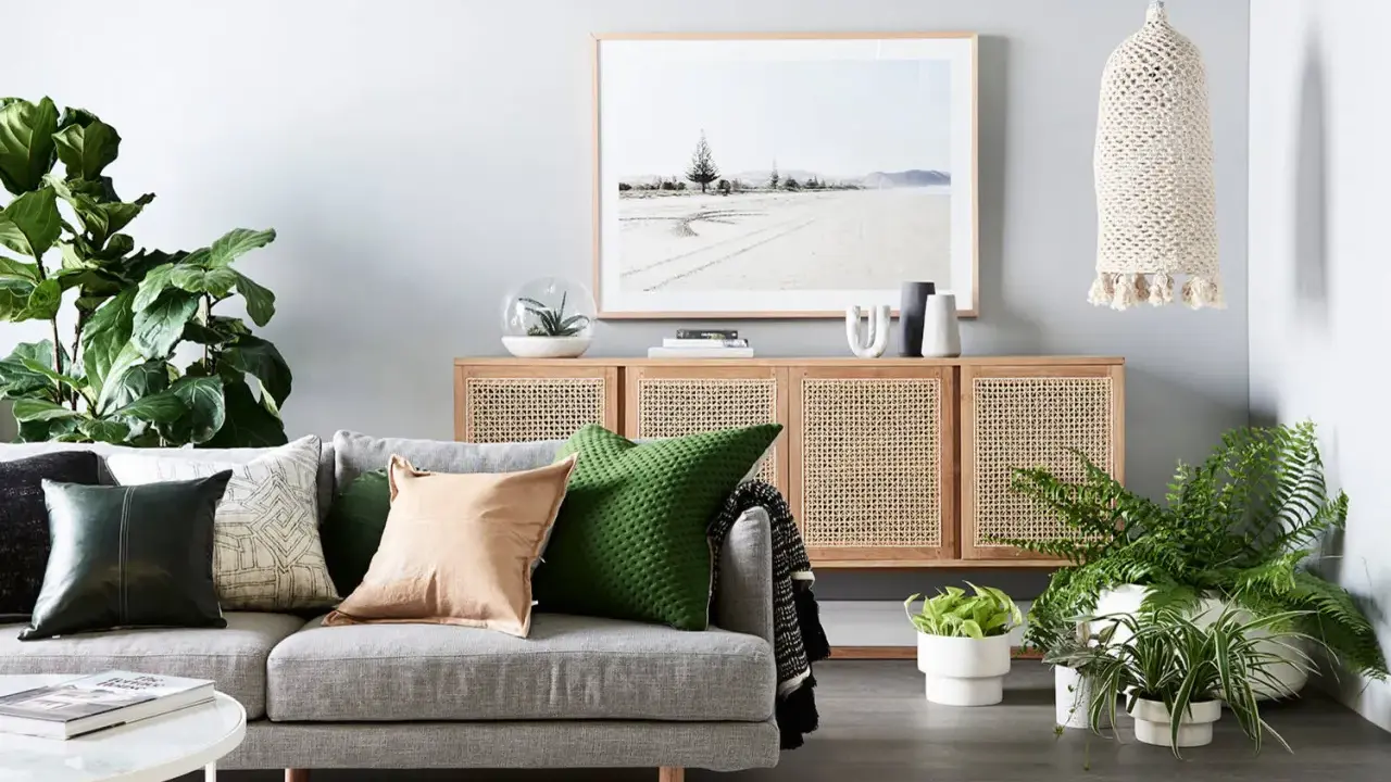 Accogliente zona giorno con divano grigio, cuscini colorati, credenza in rattan e piante verdi.