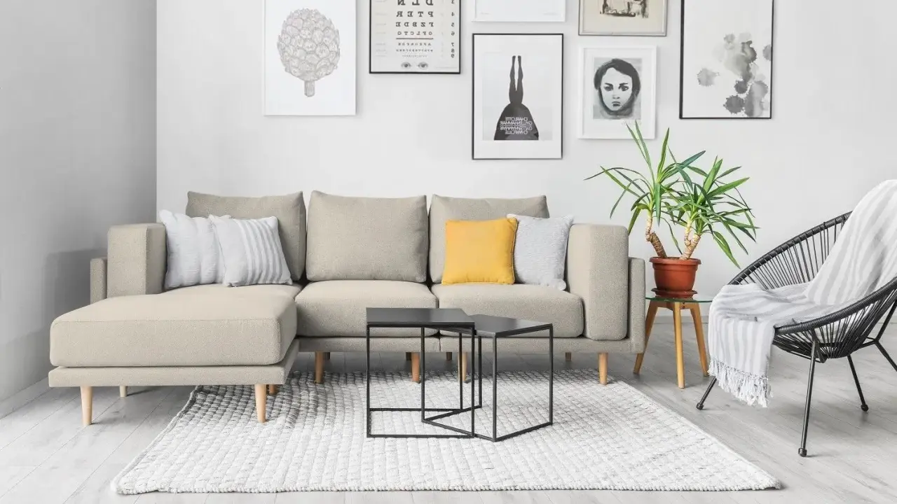 Divano componibile beige con cuscini, tavolini neri, tappeto bianco e sedia nera. Ispirazione per come foderare un divano fai da te.