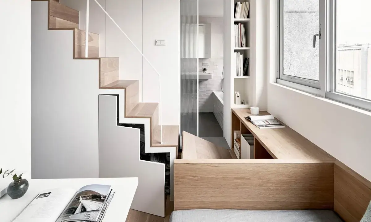 Monolocale con soppalco: scala in legno e bianco, bagno con doccia, scrivania e letto integrati.