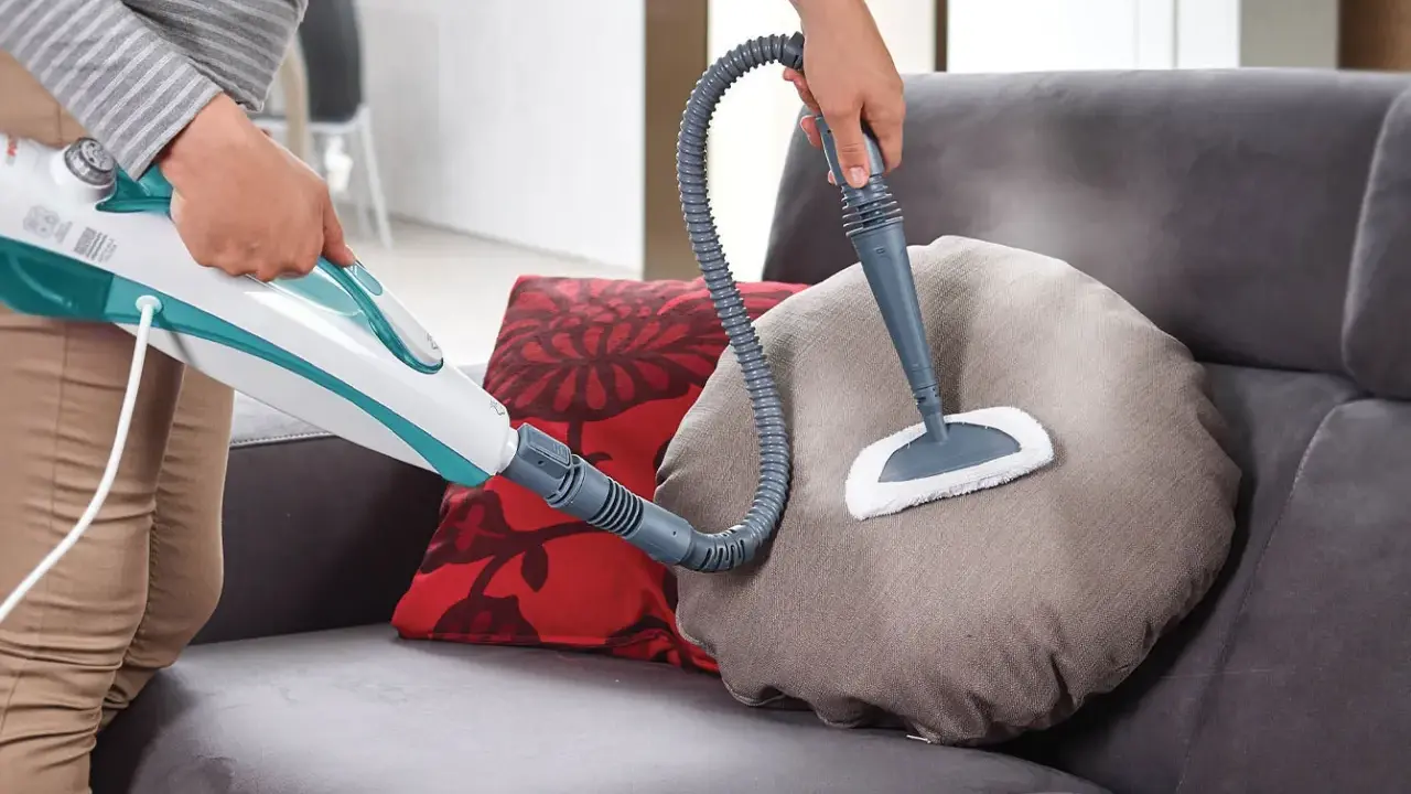 Persona pulisce un divano non sfoderabile con vaporetto, igienizzando i cuscini con vapore.