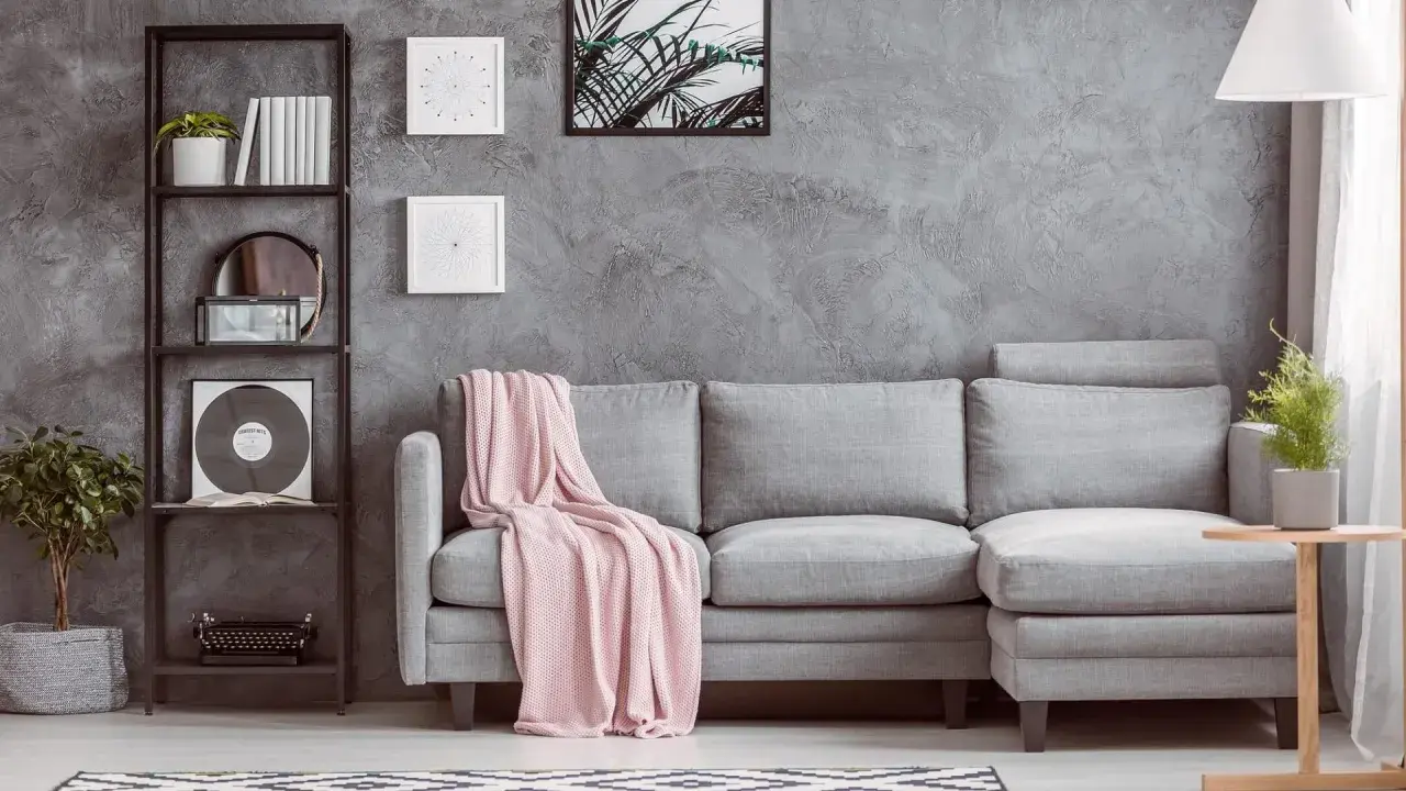 Un divano grigio con coperta rosa, una libreria nera con piante e vinile, e un tavolino di legno: ecco cosa mettere vicino al divano per un tocco di stile.