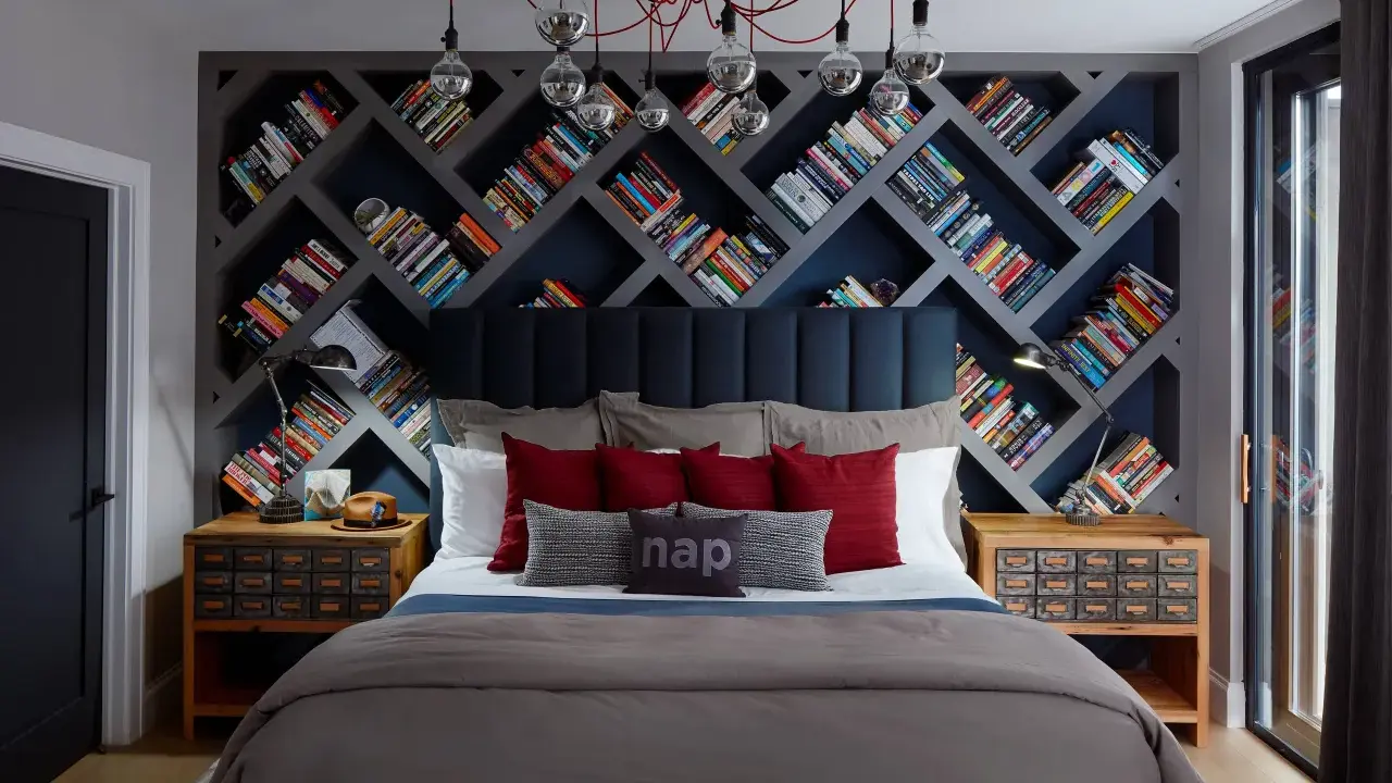 Camera da letto con un'imponente parete di librerie stravaganti a rombi, piene di libri colorati. Un letto accogliente con cuscini rossi e grigi.