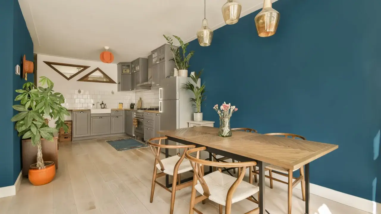 Un tavolo in legno con sedie in stile Wishbone, ideale per arredare sala da pranzo moderna. Parete blu intenso e cucina grigia completano l'ambiente.