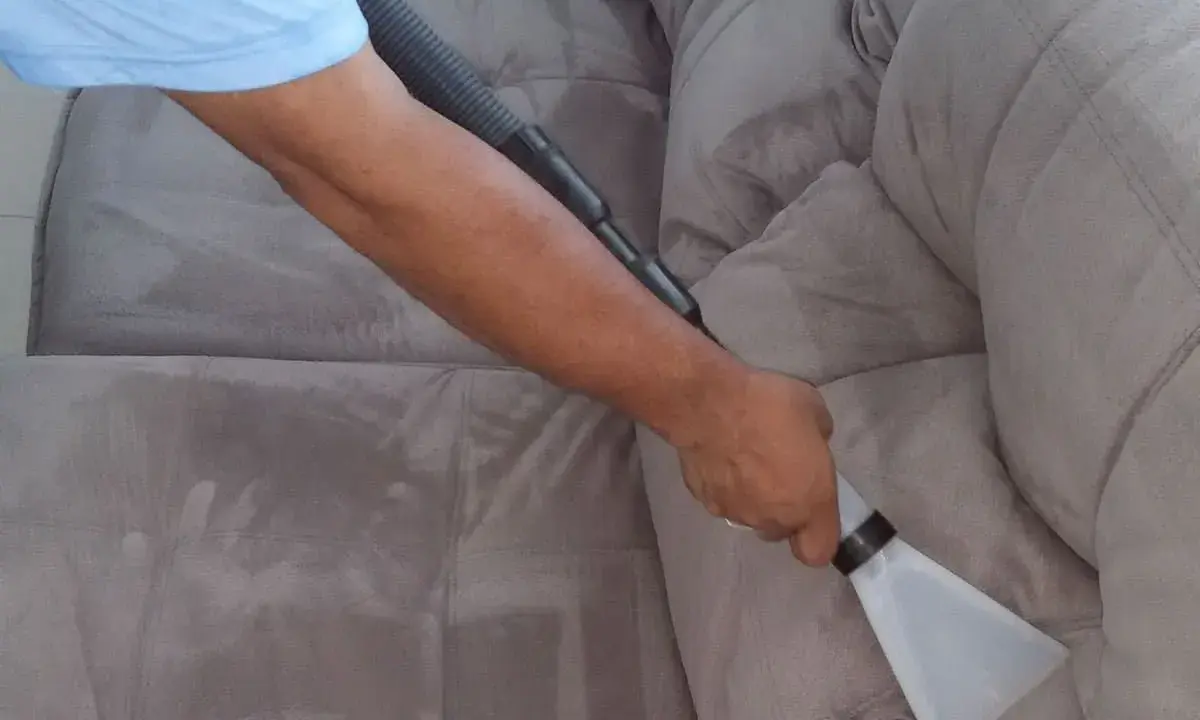 Un braccio usa un aspiratore per pulire un divano in tessuto grigio. Il processo di come pulire divano in tessuto è mostrato in dettaglio.