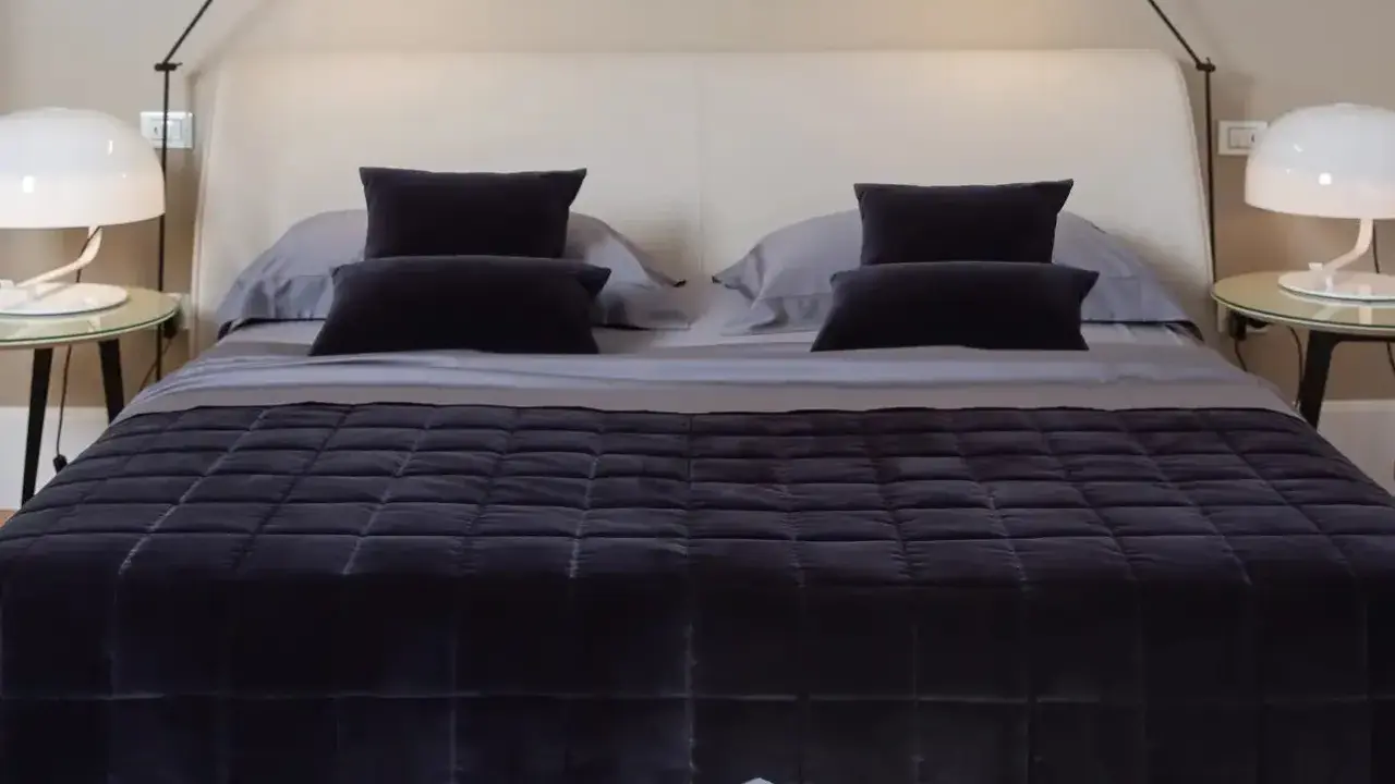 Un letto ben fatto, con copriletto trapuntato scuro e cuscini coordinati. Un esempio di come rifare il letto per un'atmosfera elegante.