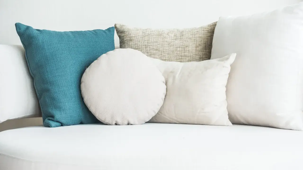 Cuscini di varie forme e colori su un divano bianco. Scopri come lavare i cuscini del divano per mantenerli freschi e puliti.