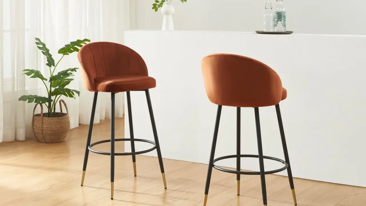 Due poltrone sgabello color ruggine, con gambe nere e dettagli dorati, in un ambiente moderno con piante e una barra.