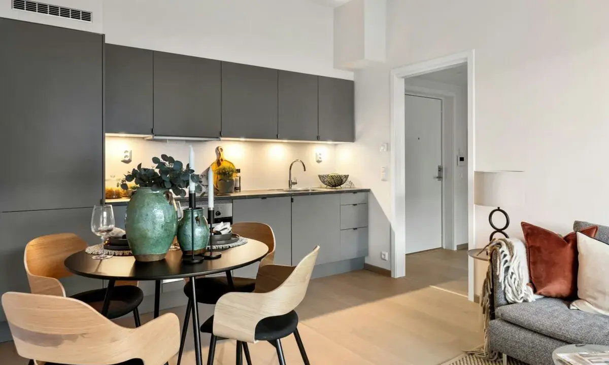 Arredare una sala moderna con cucina a vista: tavolo rotondo con sedie in legno, vasi verdi e candele.