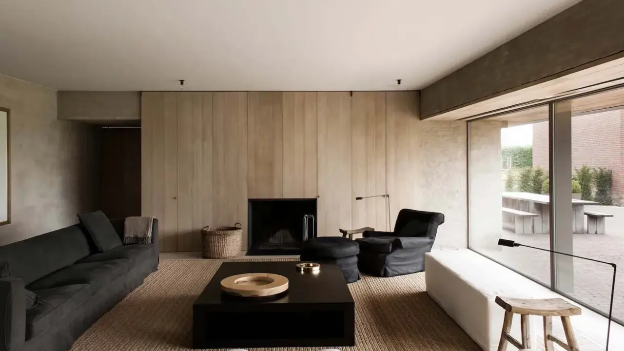 Elegante salone moderno con divani scuri, camino a parete in legno, tavolino nero e poltrona. Un esempio di come arredare un salone con stile minimalista.