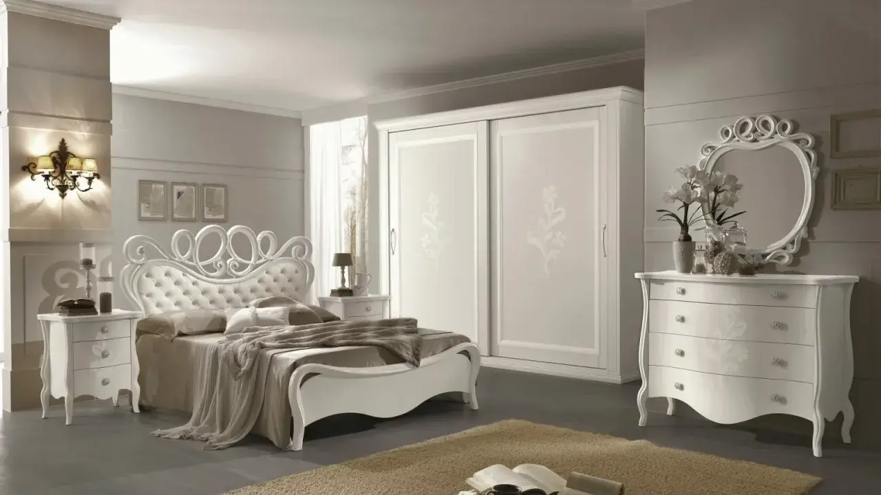 Elegante camera da letto bianca con letto capitonné, armadio scorrevole e comò con specchio. Ottime idee camera da letto bianca per un ambiente raffinato.