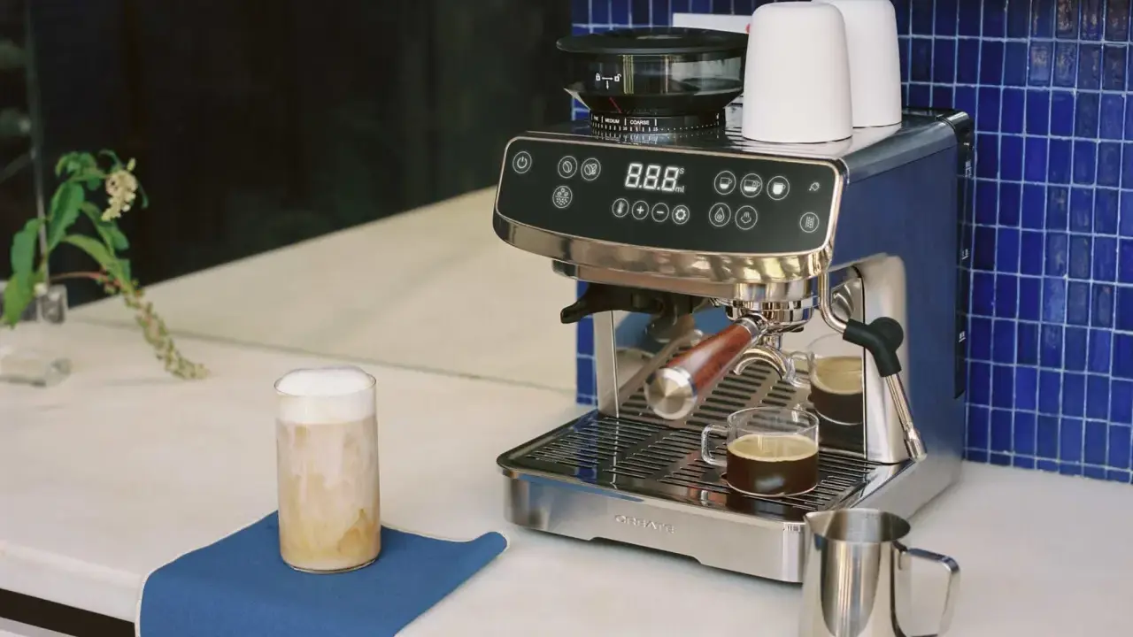Un angolo caffè casa con macchina espresso, macinacaffè, tazzine e un bicchiere di cappuccino.