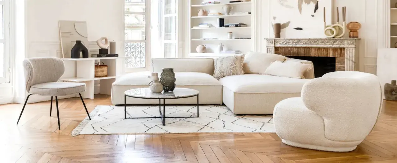 Un soggiorno luminoso con divani e design moderno. Un divano componibile bianco, una poltrona bouclé e una sedia grigia su un tappeto geometrico.