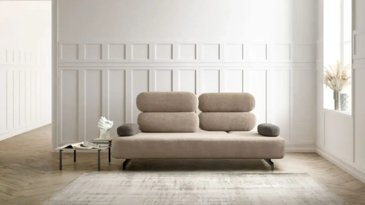 Un elegante divano beige, un'opera d'arte di design, domina la scena. Accanto, un tavolino con libri e una scultura moderna.