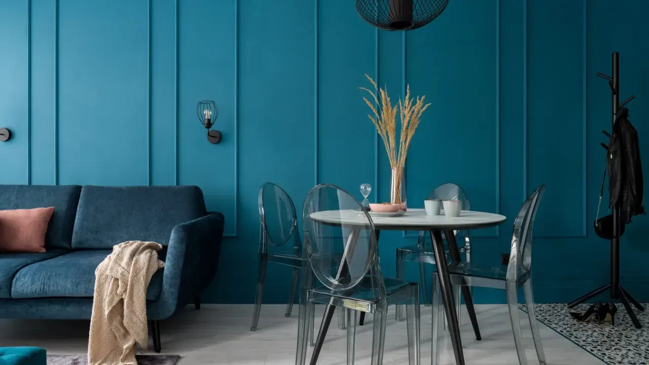 Soggiorno moderno con divano blu, tavolo rotondo con sedie trasparenti e pareti color ottanio.