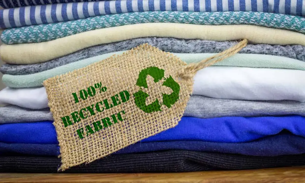 Pile di tessuti ecologici colorati, con un'etichetta che indica "100% Recycled Fabric" e il simbolo del riciclo.