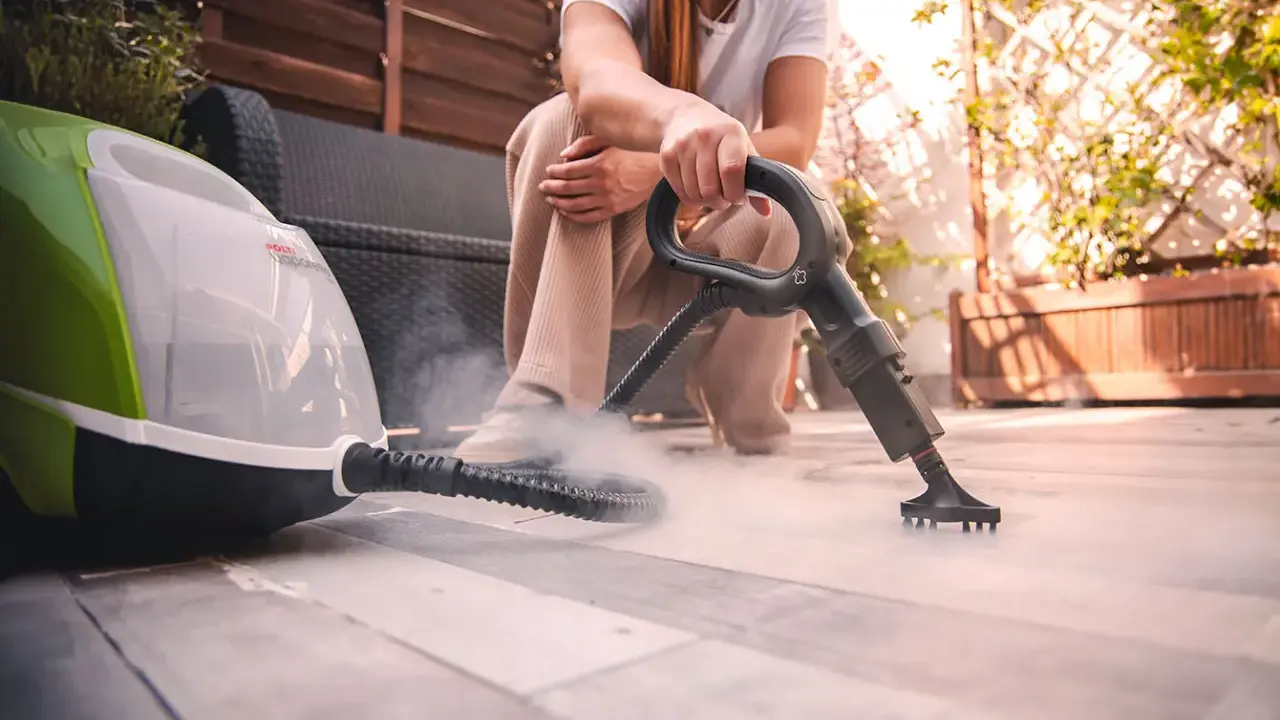 Persona usa un vaporetto per pulire la moquette esterna, creando una nuvola di vapore.