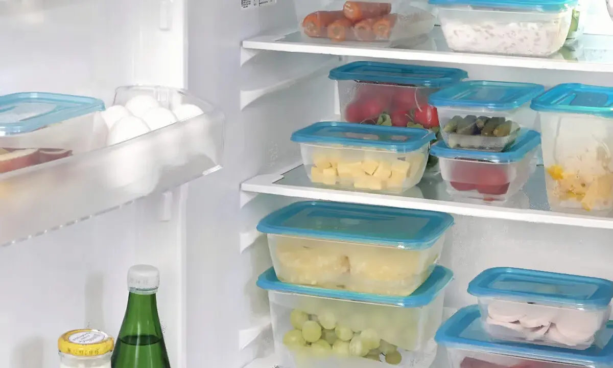 Frigo organizzato con contenitori trasparenti: carote, formaggio, cetrioli, uva, affettati. Un esempio di come organizzare il frigo per conservare al meglio gli alimenti.