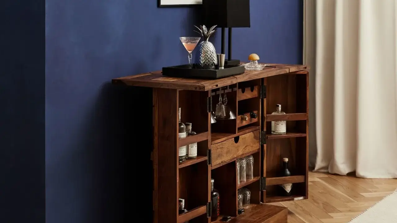 Elegante mobile bar design in legno scuro, aperto, con bottiglie, bicchieri, lampada e decorazioni.