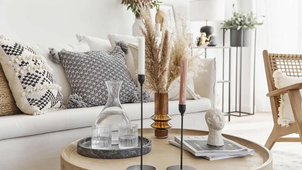 Un accogliente salotto bohemien con cuscini decorativi, un vaso di erba della pampa e candele su un tavolino rotondo.