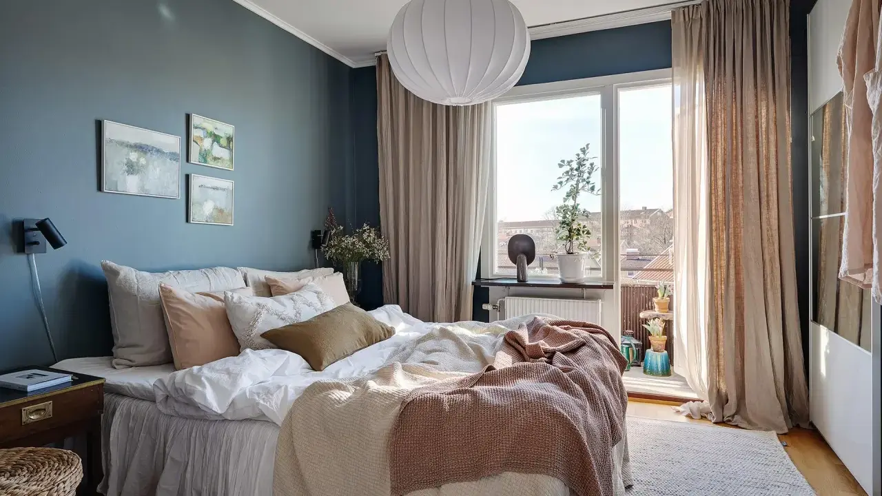Accogliente camera da letto blu e beige con letto comodo, quadri astratti e grande finestra luminosa.