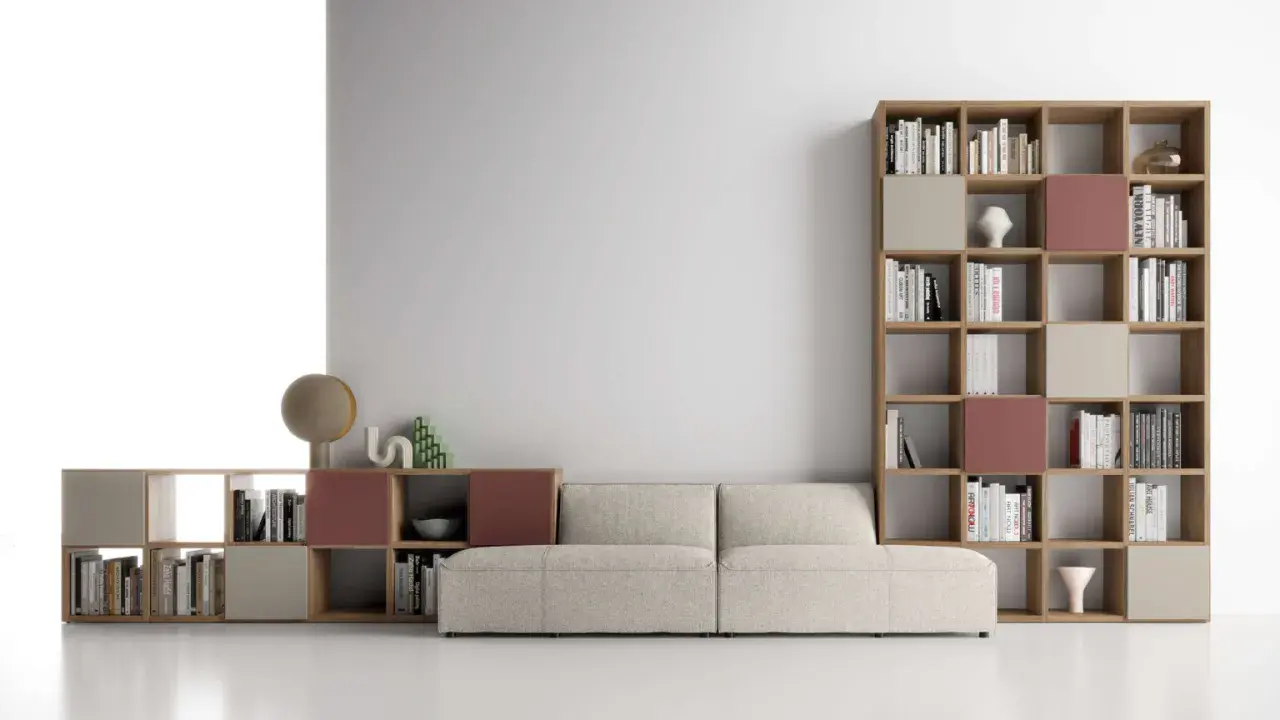 Un comodo divano beige è posizionato davanti a una libreria modulare in legno, con libri e oggetti decorativi.