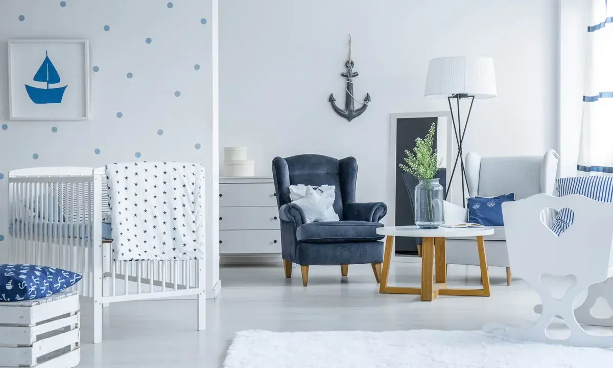 Un accogliente salotto stile marinaro con culla, poltrona blu e decorazioni a tema nautico.