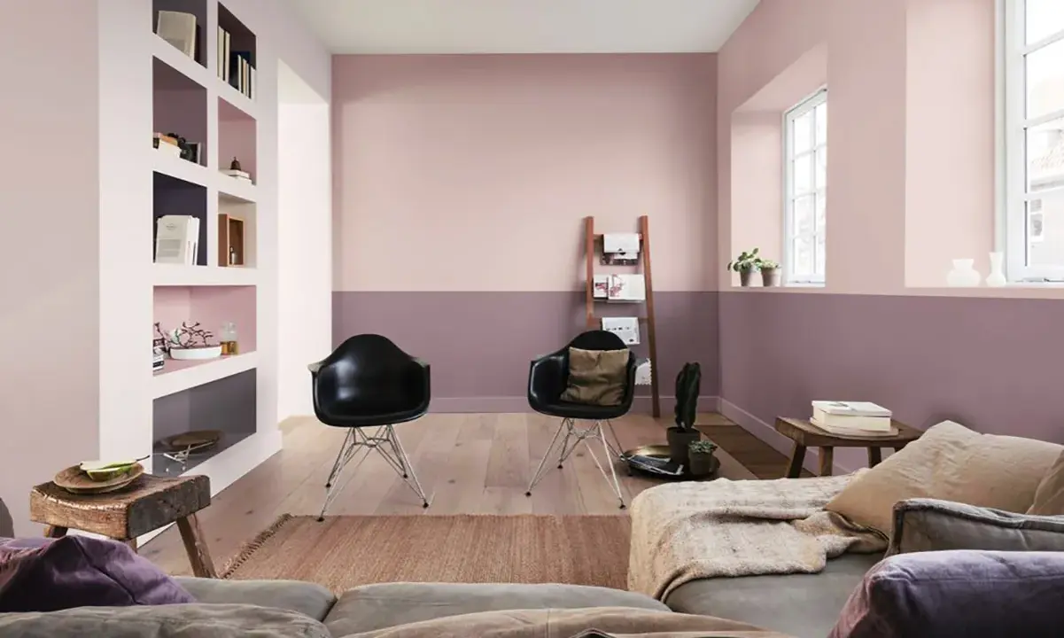 Soggiorno moderno con pareti bicolore color malva e rosa cipria, due sedie nere, divano e scaffalatura a muro.