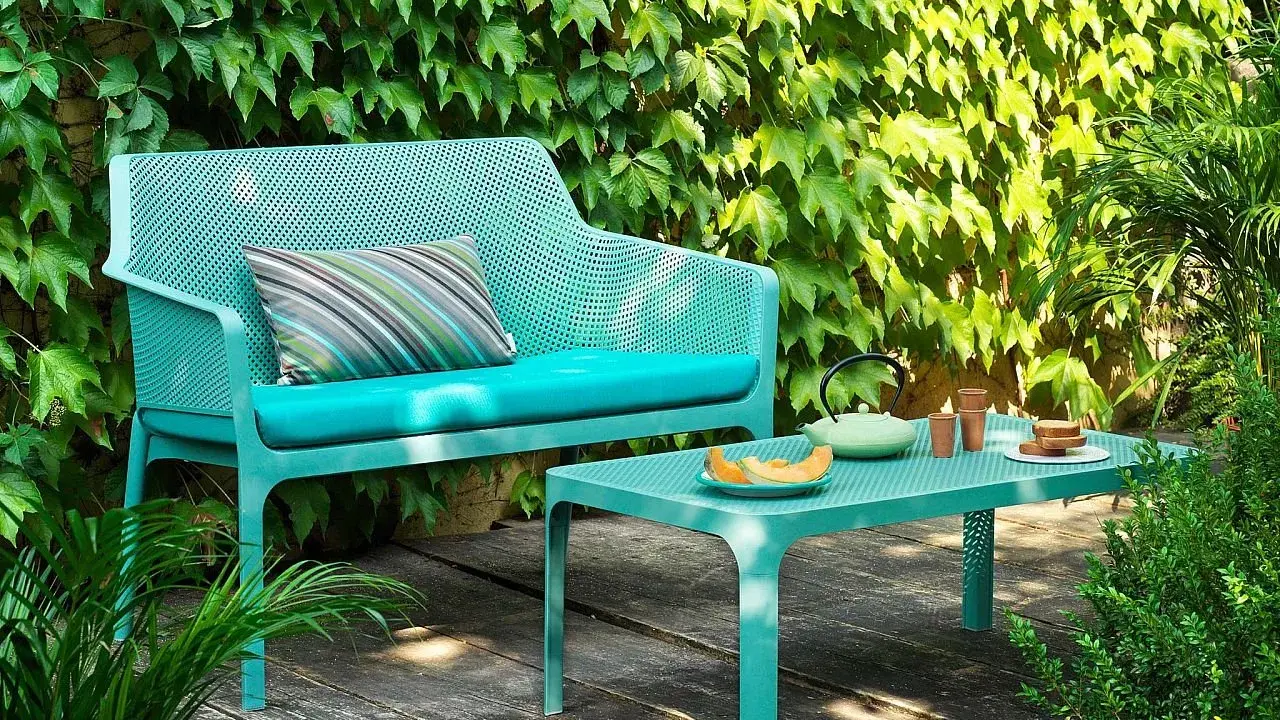 Divano e tavolino Nardi Spa Chiampo in un giardino rigoglioso, con cuscini color acqua e un set da tè.