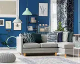 Un soggiorno moderno con divano grigio, pouf e tappeto, dominato da **colori freddi** come il blu intenso delle pareti e i toni verdi e blu degli accessori.