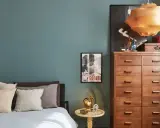 Un'elegante camera da letto con pareti color ottanio, un letto con cuscini in lino e un comò in legno. L'abbinamento colori camera da letto è sofisticato e rilassante.