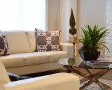 Divano in pelle bianco, con cuscini decorativi. Un tavolino di vetro con piante e libri. Ideale per chi cerca come pulire divano pelle bianco ingiallito.