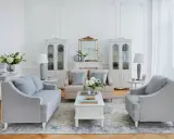 Elegante salotto shabby chic moderno con divani grigi, poltrone, tavolino bianco, specchio dorato e vetrine.