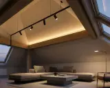 Accogliente mansarda con tetto spiovente, illuminazione soffusa e travi a vista. Un moderno sistema di faretti illumina l'ambiente, creando un'atmosfera calda e rilassante.