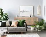 Accogliente zona giorno con divano grigio, cuscini colorati, credenza in rattan e piante verdi.