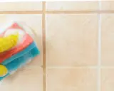 Mano con guanto giallo pulisce piastrelle del bagno con spugna schiumosa.