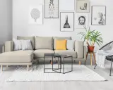 Divano componibile beige con cuscini, tavolini neri, tappeto bianco e sedia nera. Ispirazione per come foderare un divano fai da te.