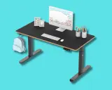 Tavolino gaming nero regolabile in altezza, con monitor, tastiera, mouse, porta penne e zainetto azzurro appeso.
