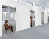 Una donna seduta in una stanza riflette in un grande specchio semiriflettente. Altre donne appaiono riflesse in specchi successivi.