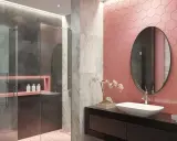 Bagno moderno con pareti rosa a nido d'ape, doccia grigia e marmo. Un lavabo ovale su mobile nero e specchio rotondo completano queste idee bagno rosa.