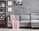 Un divano grigio con coperta rosa, una libreria nera con piante e vinile, e un tavolino di legno: ecco cosa mettere vicino al divano per un tocco di stile.