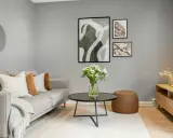 Un accogliente salotto piccolo con divano grigio, tavolino nero, pouf marrone e quadri astratti alle pareti.
