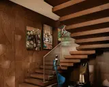 Elegante interior design casa con pareti in legno intagliato a ventaglio, quadri astratti e una scala sospesa in legno.