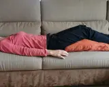 Donna sdraiata sul divano con un cuscino sotto le ginocchia per una postura corretta seduti divano.