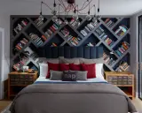 Camera da letto con un'imponente parete di librerie stravaganti a rombi, piene di libri colorati. Un letto accogliente con cuscini rossi e grigi.