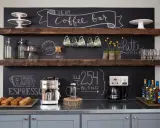 Un angolo caffè fai da te con macchine, tazze, muffin e scritte alla lavagna.