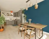 Un tavolo in legno con sedie in stile Wishbone, ideale per arredare sala da pranzo moderna. Parete blu intenso e cucina grigia completano l'ambiente.