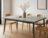 Un elegante tavolo minimal design con piano in cemento e sedie in legno chiaro. Un vaso con rami secchi e due libri completano l'arredo.